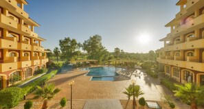A hotel courtyard with a swimming pool, palm trees, and a gazebo. - Hotel ILUNION Golf Badajoz (Badajoz)