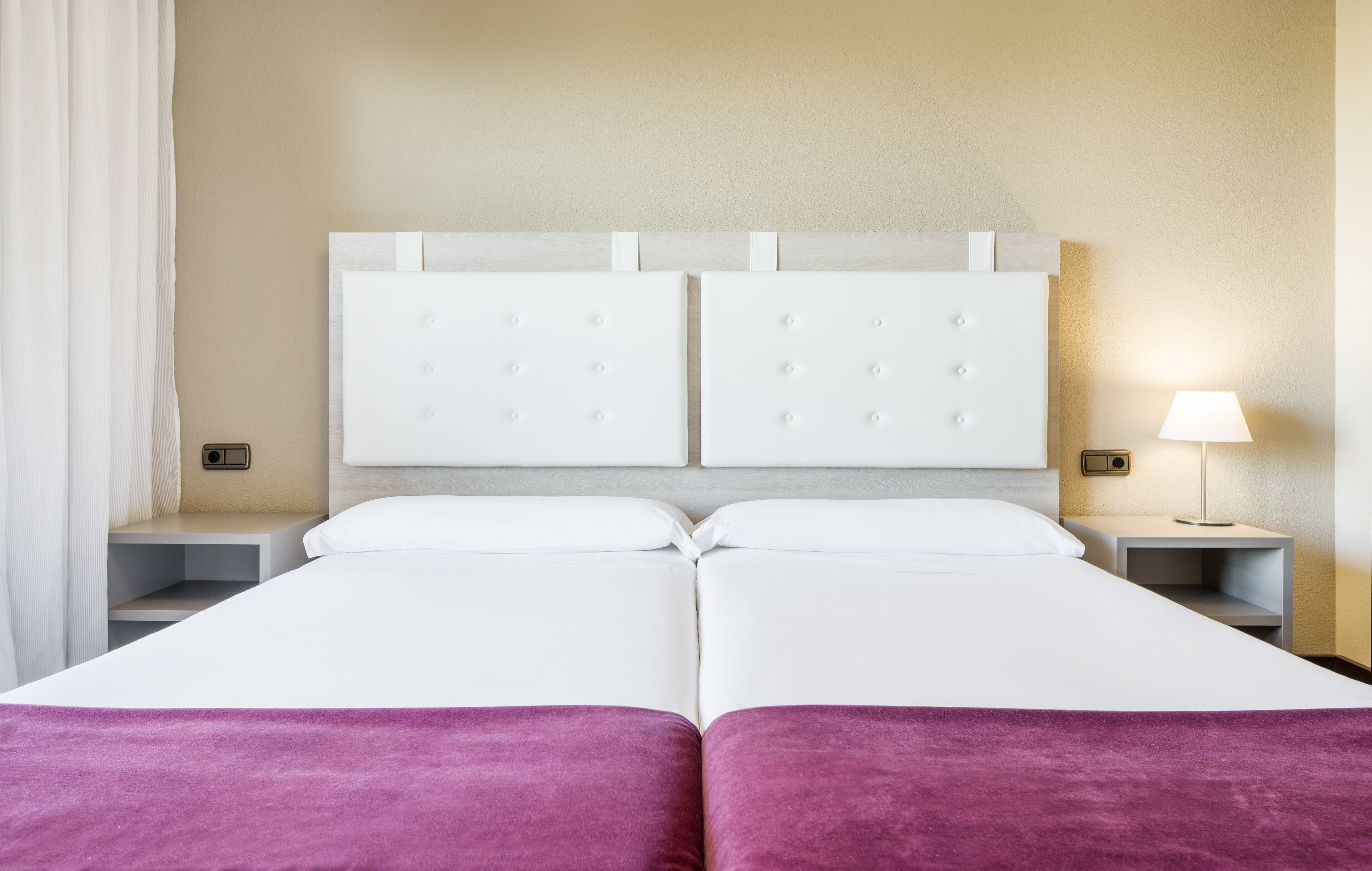 A double bed with a headboard, two bedside tables, a lamp, and a purple throw blanket.