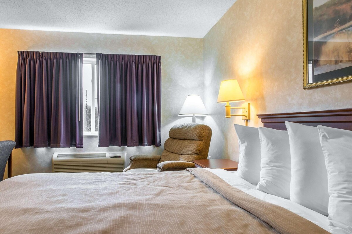 A hotel room with a bed, a chair, a lamp, and a window with curtains.