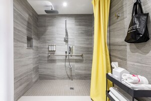 Un espace douche moderne avec une porte en verre, un porte-serviettes avec des serviettes et un sac noir aux couleurs de l’hôtel.