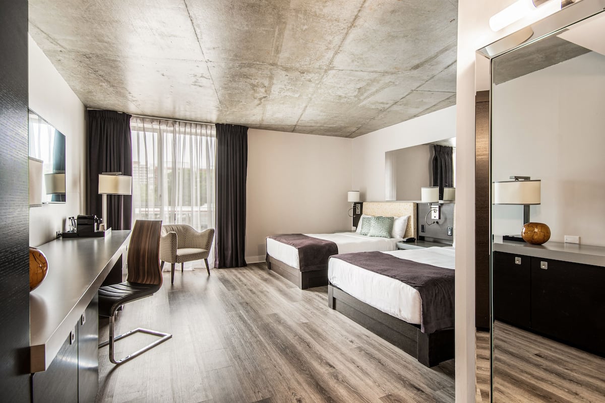 Une chambre d’hôtel moderne avec un plafond en béton, deux lits, un bureau et une chaise.