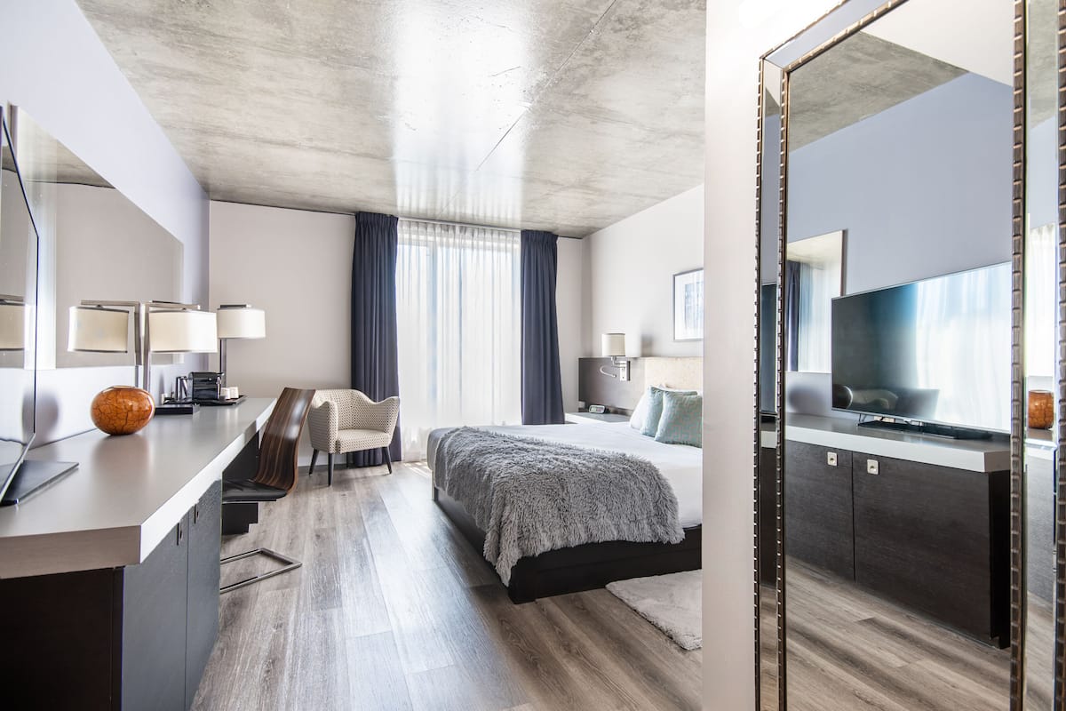 Une chambre d’hôtel moderne, équipée d’un lit, d’une table de chevet, d’une lampe et d’un grand miroir.