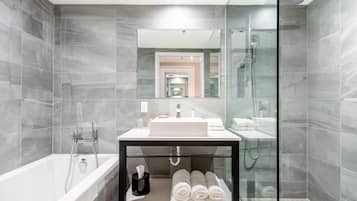 Un baño moderno con ducha envuelta en vidrio, un lavamanos blanco y un tocador negro con toallas.