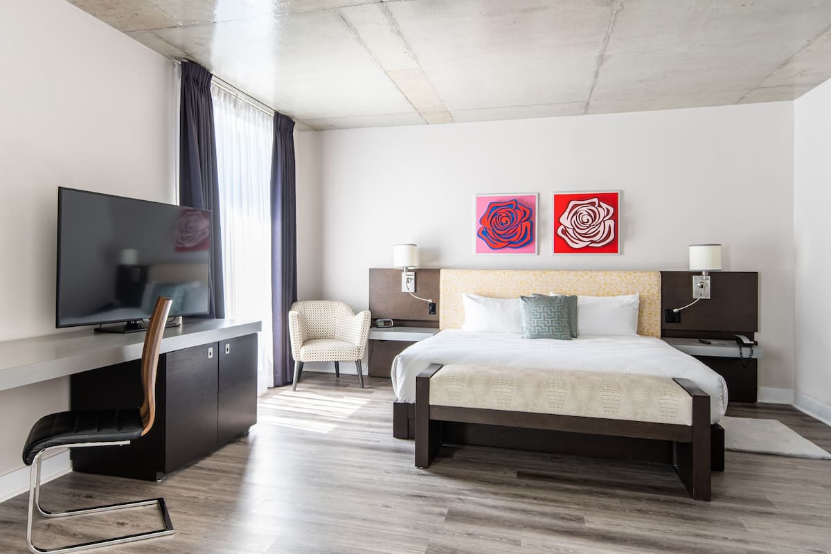 Une chambre d’hôtel moderne équipée d’un lit, d’un bureau avec une télévision, d’une chaise et de deux lampes fixées au mur.