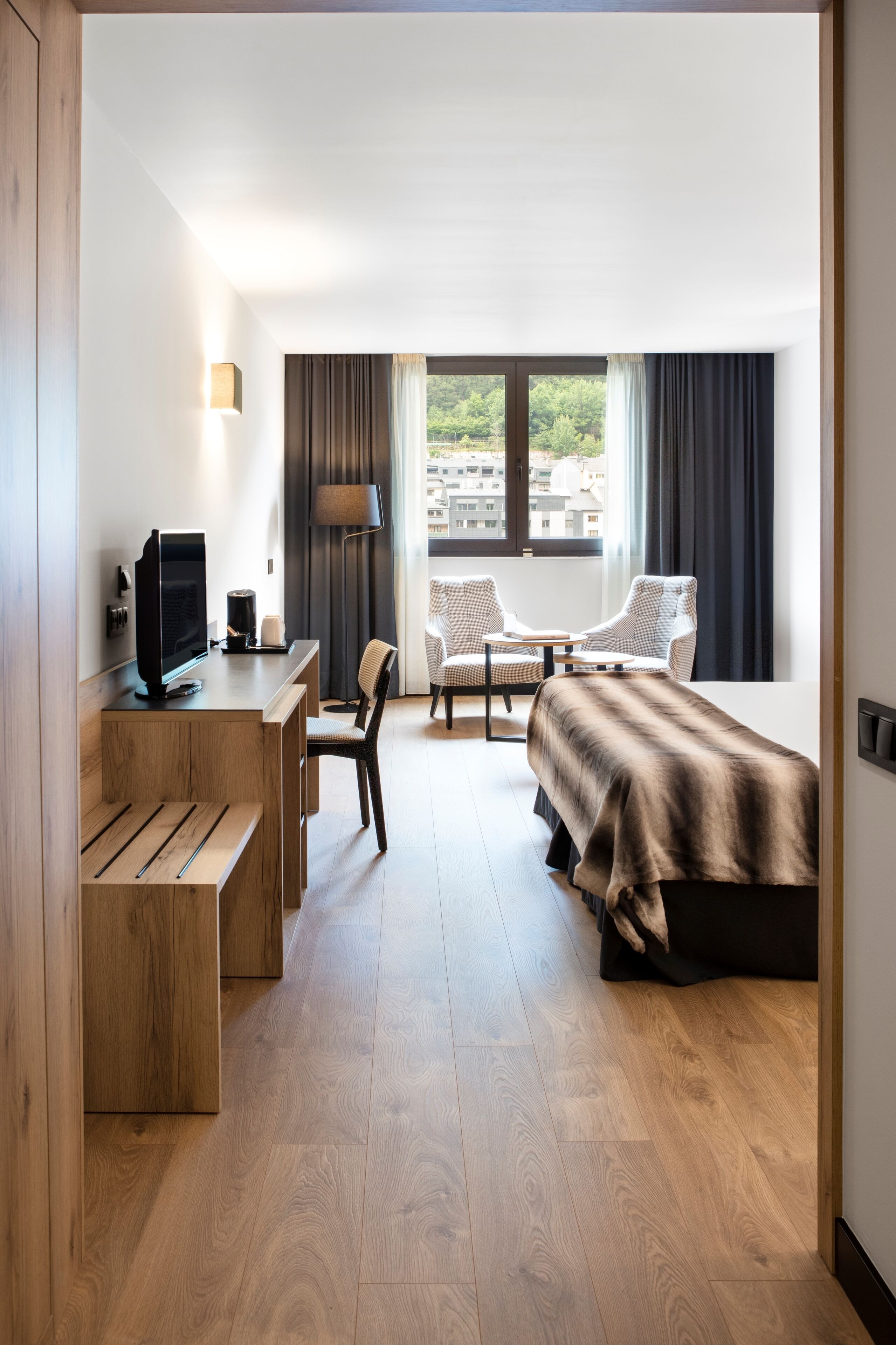 Une chambre d’hôtel moderne avec un bureau en bois, un lit et deux chaises.
