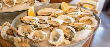 A metal bowl filled with oysters on ice, with a lemon wedge visible.