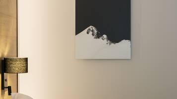Une chambre à coucher avec un lit, des oreillers, une lampe fixée au mur et un tableau représentant une montagne.