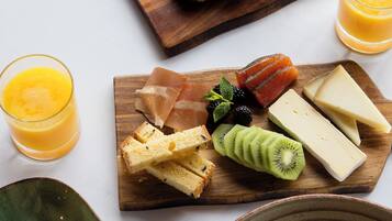 Ein Frühstückstisch mit Holzbrett, belegt mit Gebäck, Käse, Räucherlachs und Obst. Dazu zwei Gläser Orangensaft und ein Teller mit Eiern und Butter.