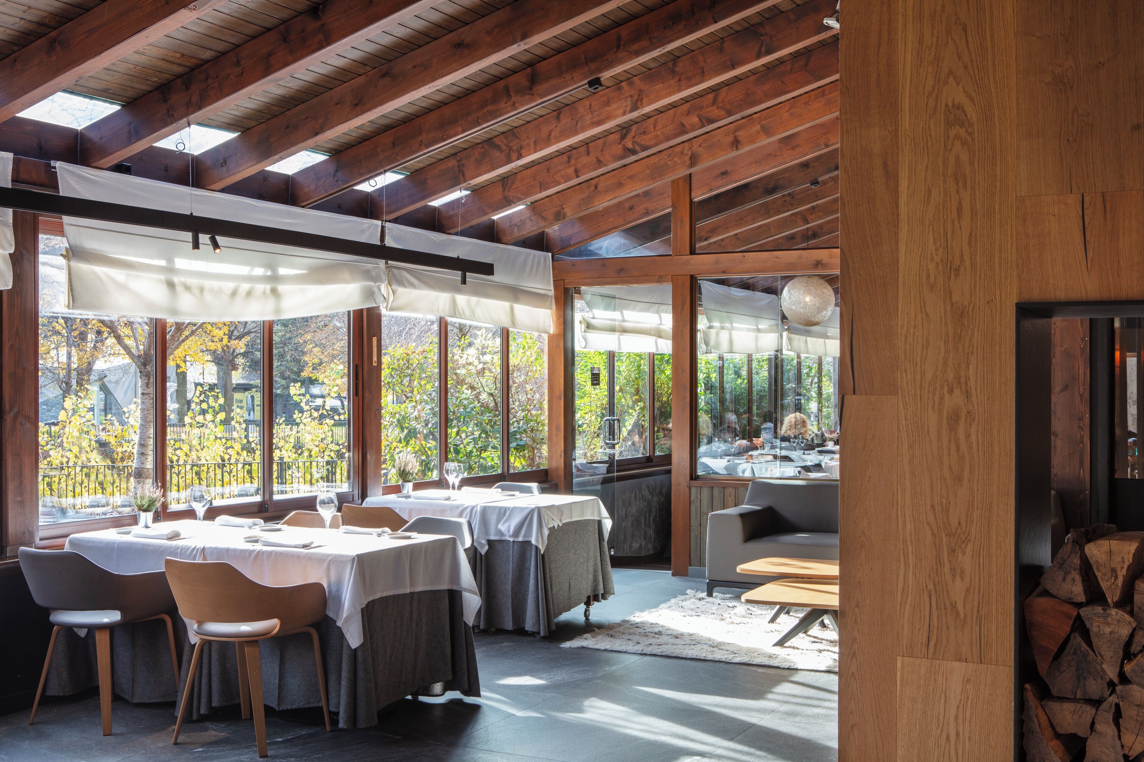 Comedor con mesas y sillas, ventanas amplias y vistas a árboles.