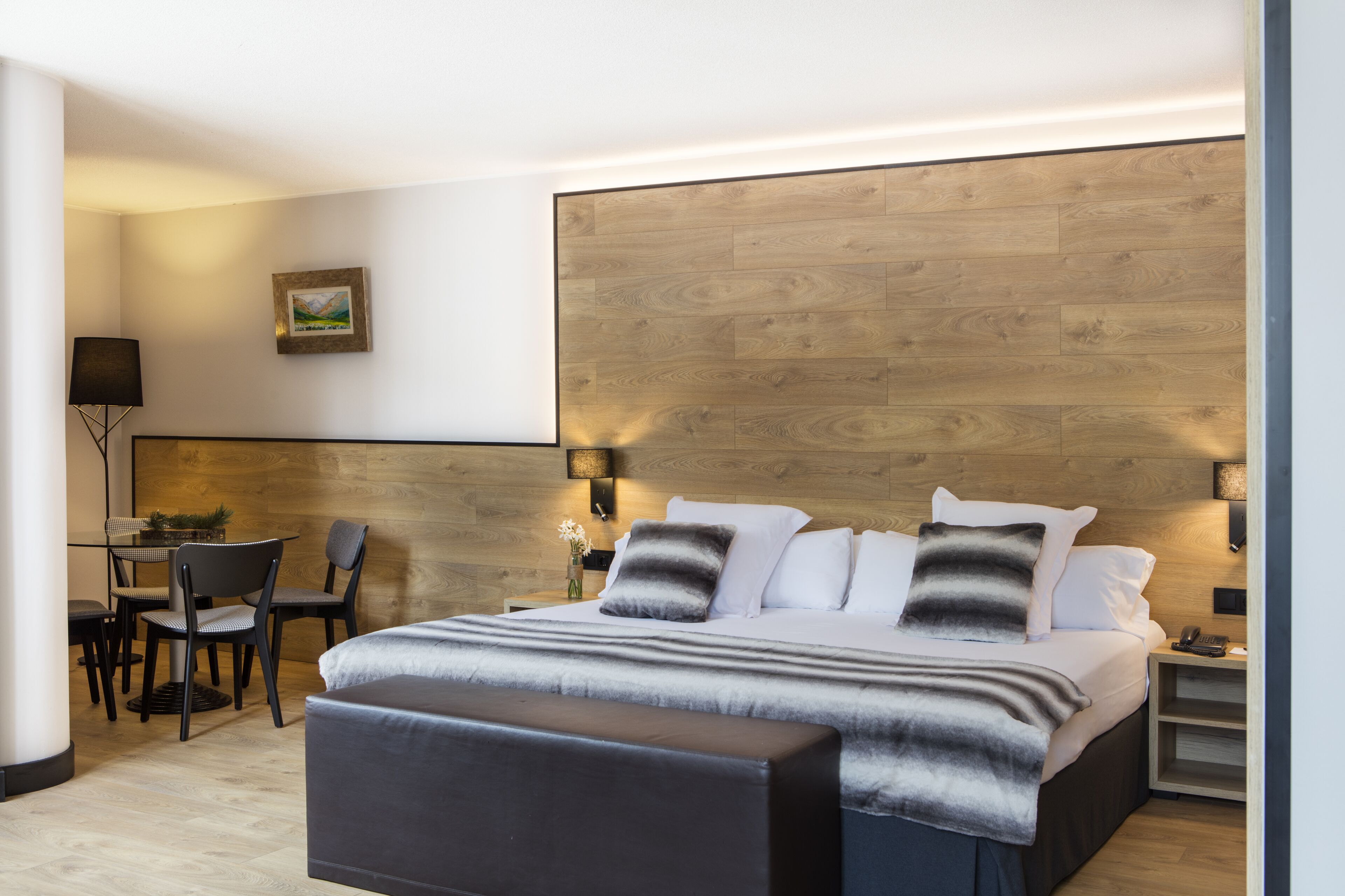 Een moderne hotelkamer met een groot bed, een bureau met stoelen en een houten accentmuur.
