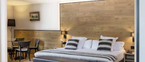Una habitación de hotel moderna con una cama grande, un escritorio con sillas y una pared de detalles en madera.