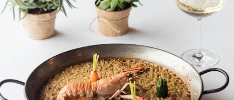 A seafood dish in a pan, a glass of white wine, and small potted plants on a table.