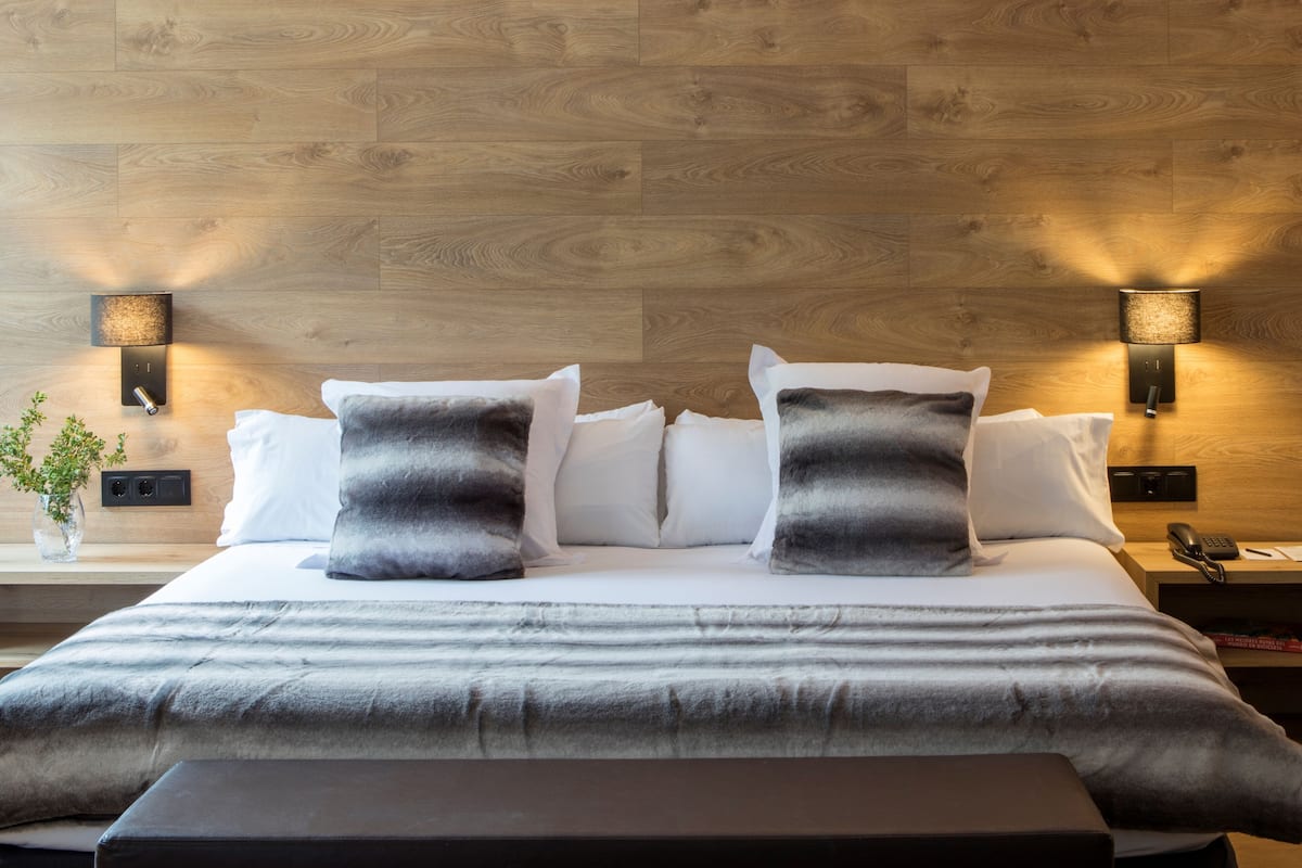 A neatly made bed with a grey and white duvet, two grey pillows, and a black bedside table with a lamp.