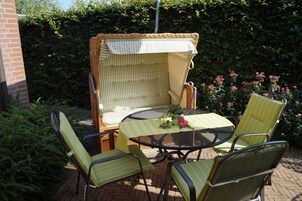 Una silla de mimbre con un cojín blanco, una mesa redonda con mantel verde y dos sillas verdes con cojines a rayas.