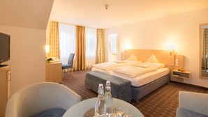 Ein Hotelzimmer mit einem Bett, zwei Nachttischen, einem Sessel, einem Schreibtisch und einem Fernseher.