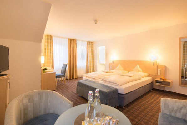 A hotel room with a bed, two bedside tables, a chair, a desk, and a television.
