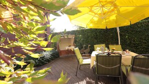 Eine Terrasse im Freien mit einem gelben Sonnenschirm, Korbmöbeln und einem Backsteinboden.