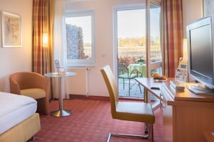 Habitación de hotel con cama, escritorio con computadora, silla, una mesita y ventana con vista al exterior.