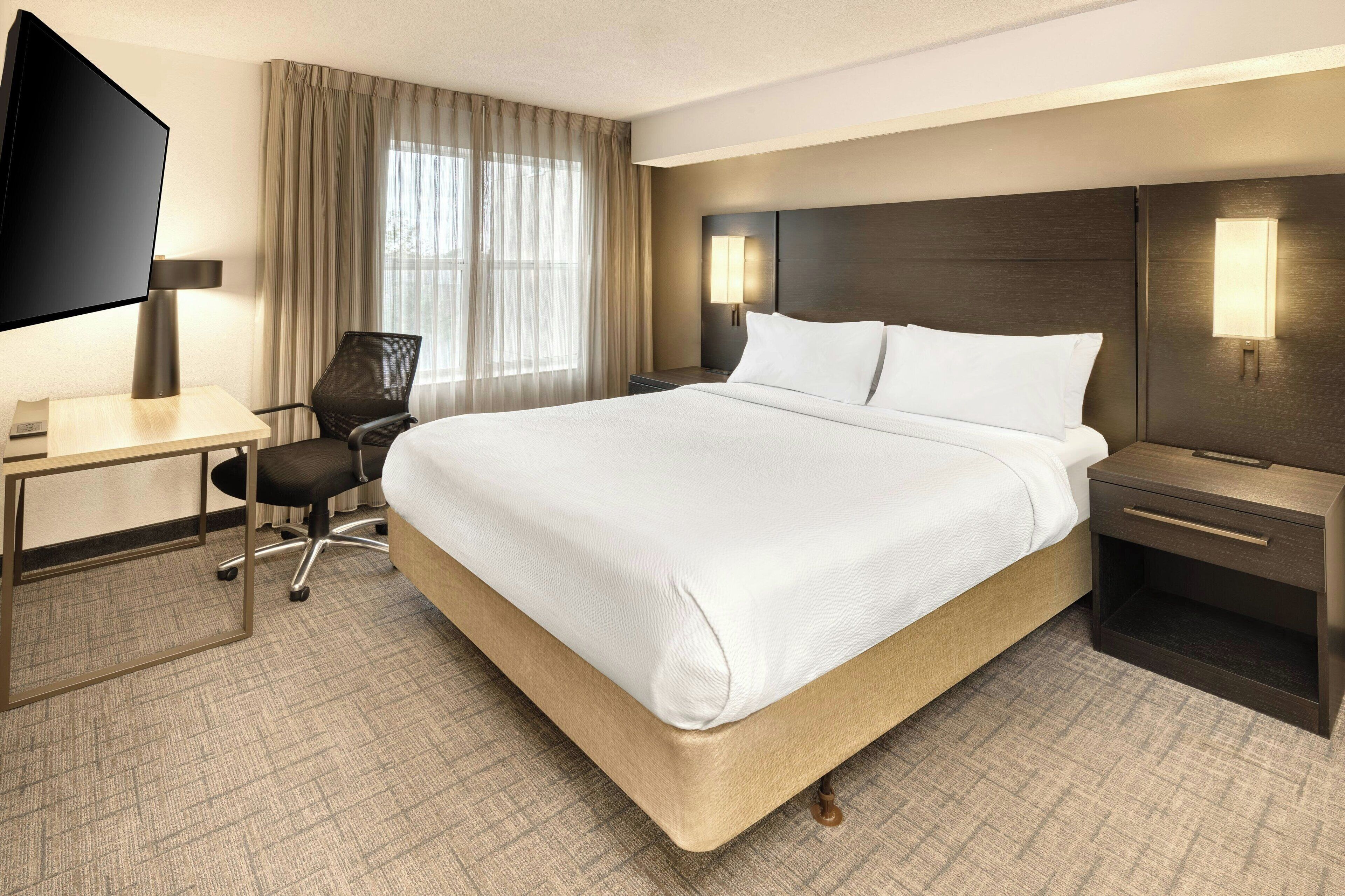 Une chambre d’hôtel avec un grand lit, un bureau doté d’un téléviseur à écran plat, une chaise et une table de chevet avec une lampe.