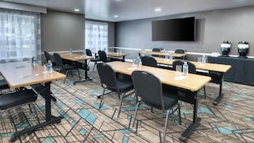 A conference room with multiple tables and chairs, water bottles, and a large flat-screen TV on the wall.