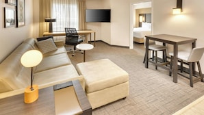 A hotel room with a sofa, ottoman, desk, chairs, a flat-screen TV, and a bed. - Residence Inn by Marriott Whitby (Whitby)