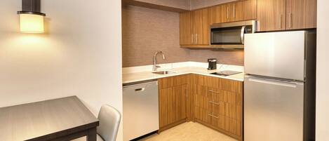 A compact kitchen with wooden cabinets, a stainless steel refrigerator, a microwave, and a dishwasher.
