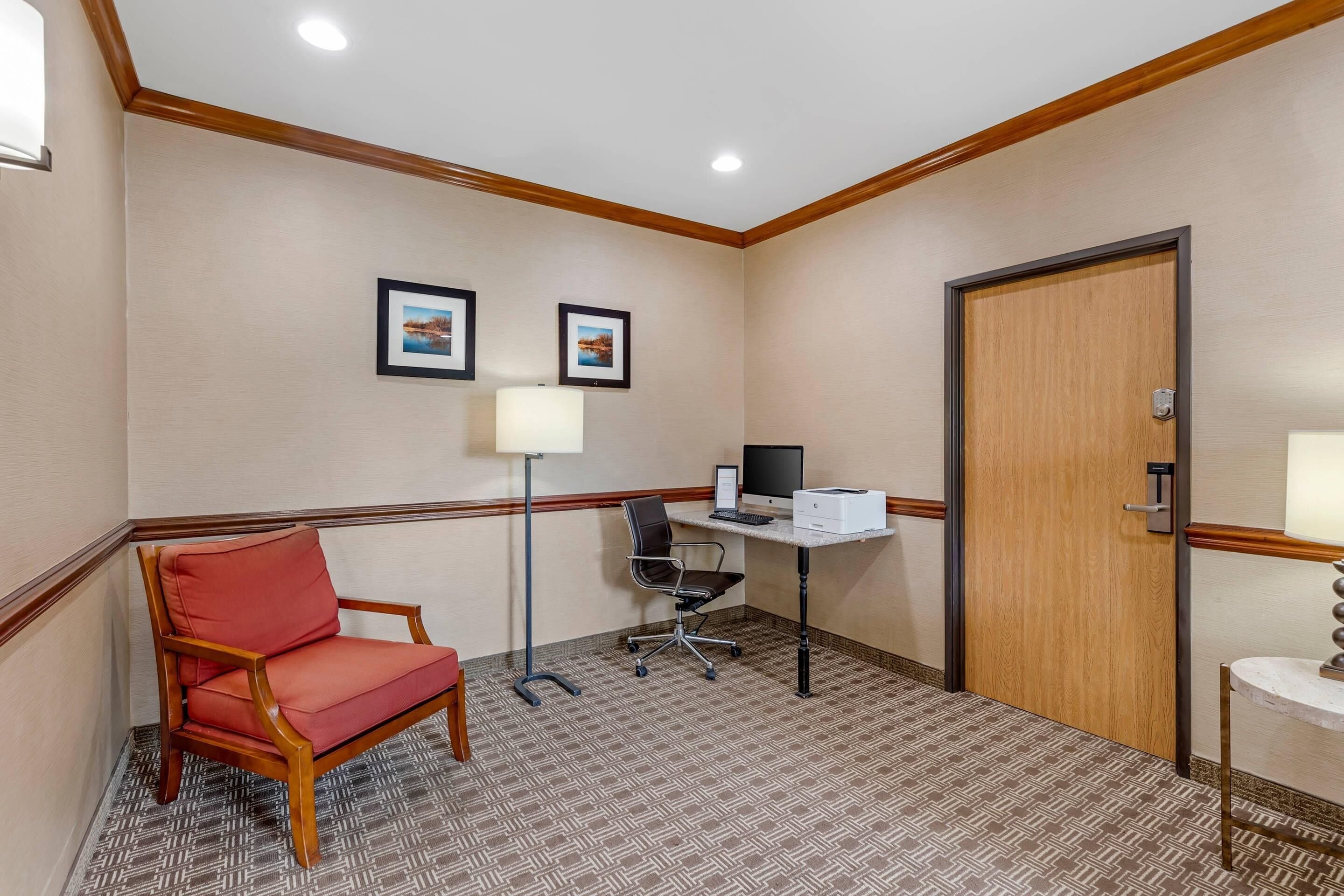 A hotel room with a wooden chair, desk, computer, and two framed pictures on the wall.
