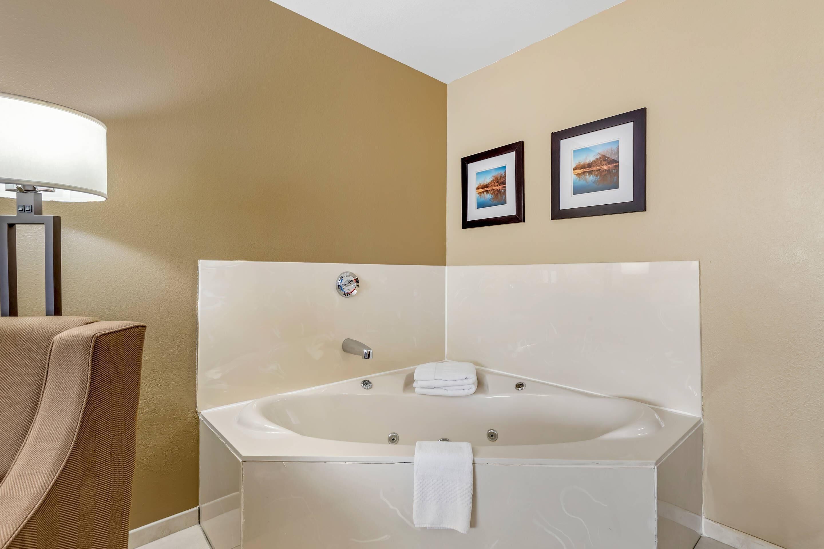 A modern bathroom with a large bathtub, a towel rack, and two framed pictures on the wall.