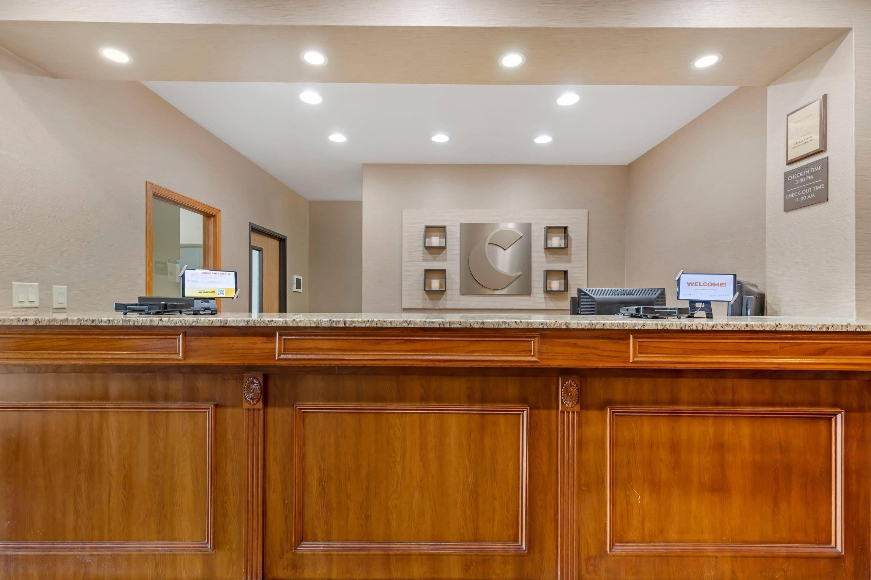 A hotel reception desk with a wooden panel design, a digital check-in kiosk, and a wall-mounted clock.