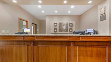 A hotel reception desk with a wooden panel design, a digital check-in kiosk, and a wall-mounted clock.