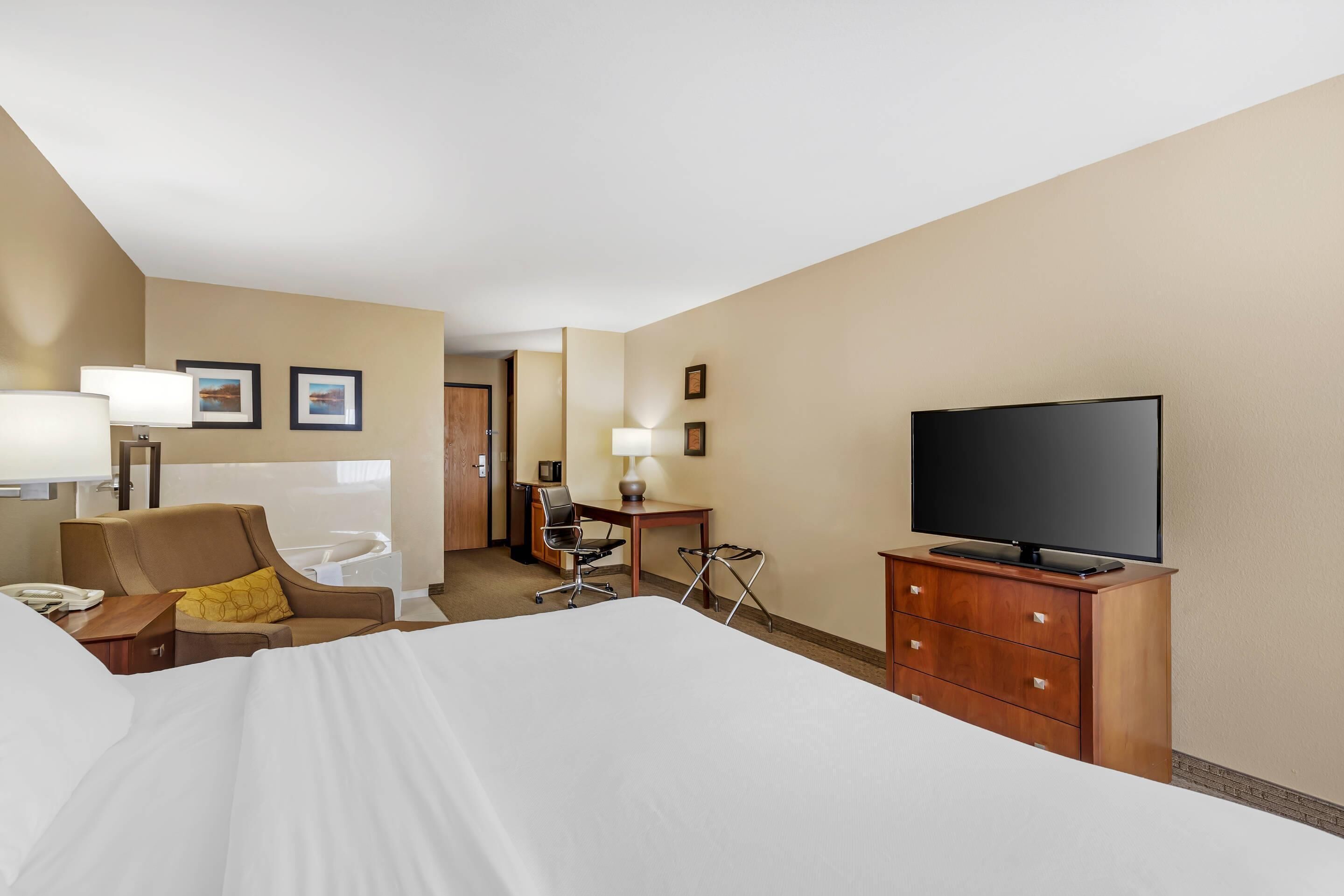 A hotel room with a large bed, a desk with a chair, a television, and a desk lamp.