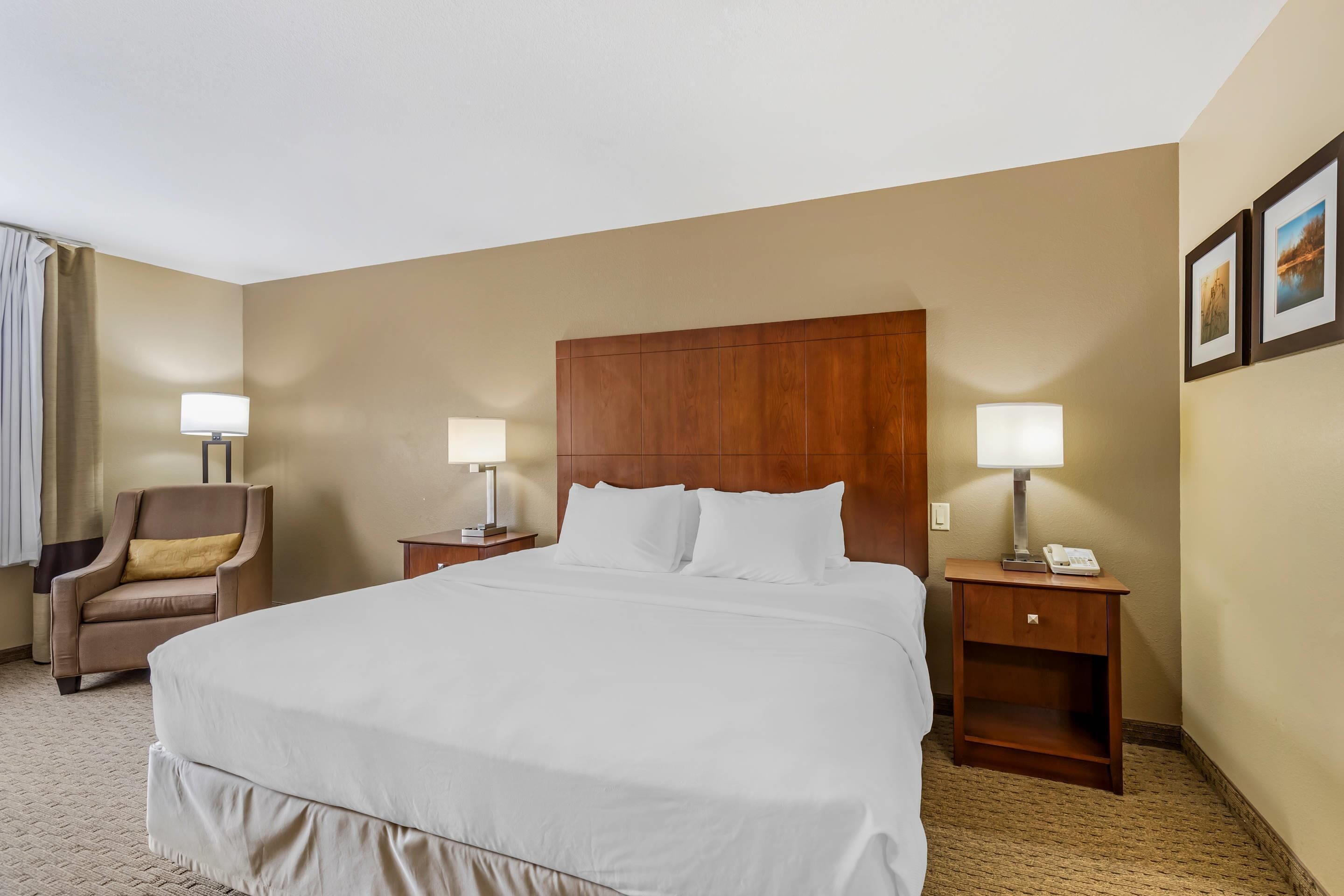 Habitación de hotel con una cama grande, dos mesitas de noche con lámparas, una silla y un cabecero de madera.