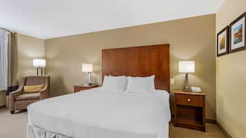 A hotel room with a large bed, two bedside tables with lamps, a chair, and a wooden headboard.