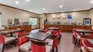 A hotel dining area with multiple tables and chairs, a buffet station, and a refrigerator.