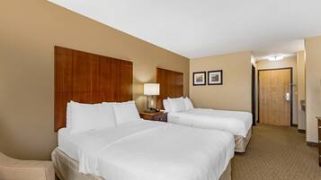 A hotel room with two beds, a wooden headboard, a nightstand, a lamp, and a door.