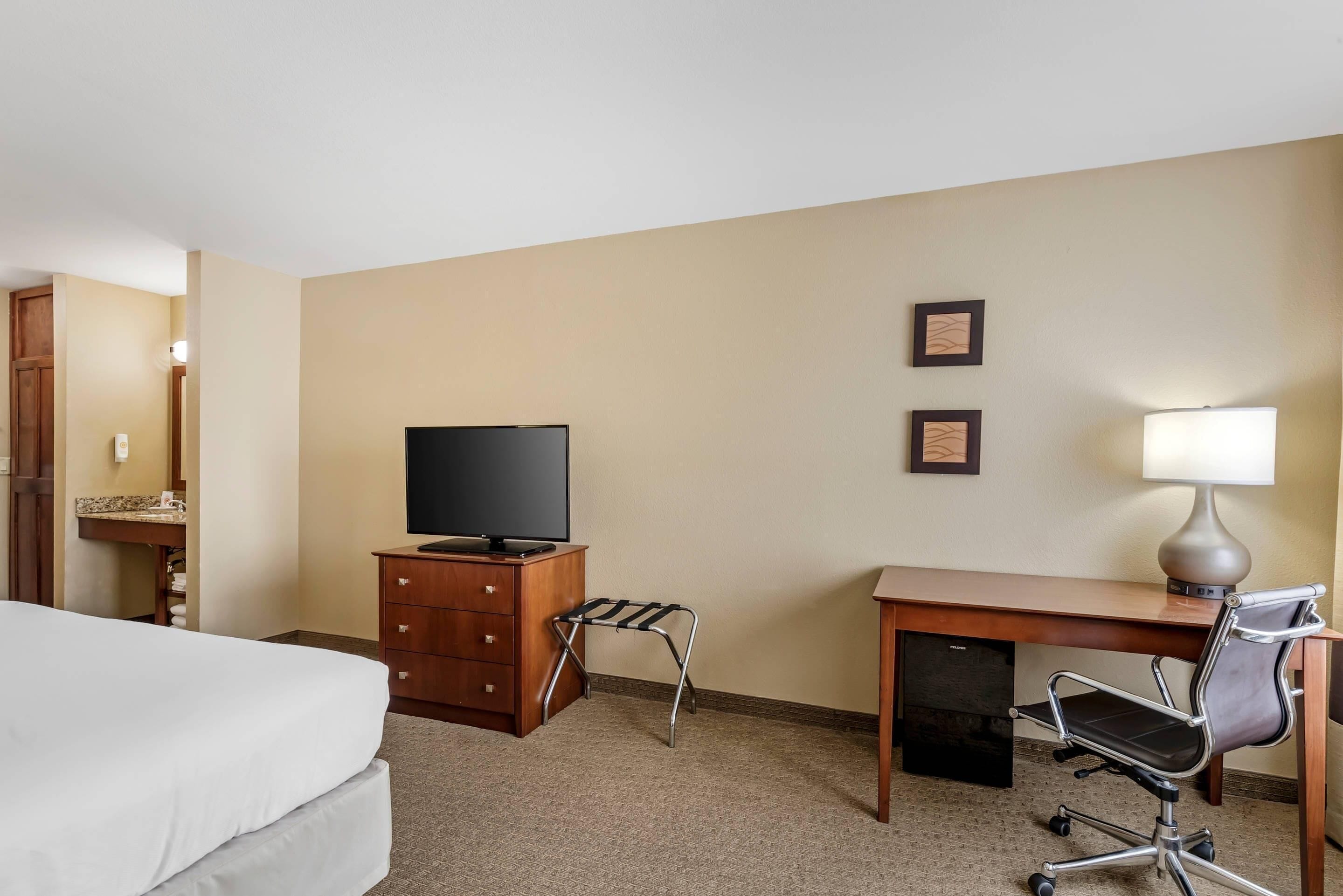 A hotel room with a bed, a desk with a chair, a television, and a lamp.