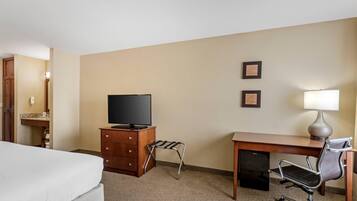 A hotel room with a bed, a desk with a chair, a television, and a lamp.
