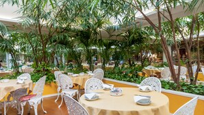 A restaurant with round tables, white chairs, and a tropical plant canopy. - Hotel Venezia (Mestre)