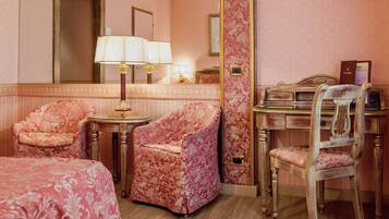 A hotel room with two pink upholstered chairs, a wooden desk, and a bed with a pink bedspread.