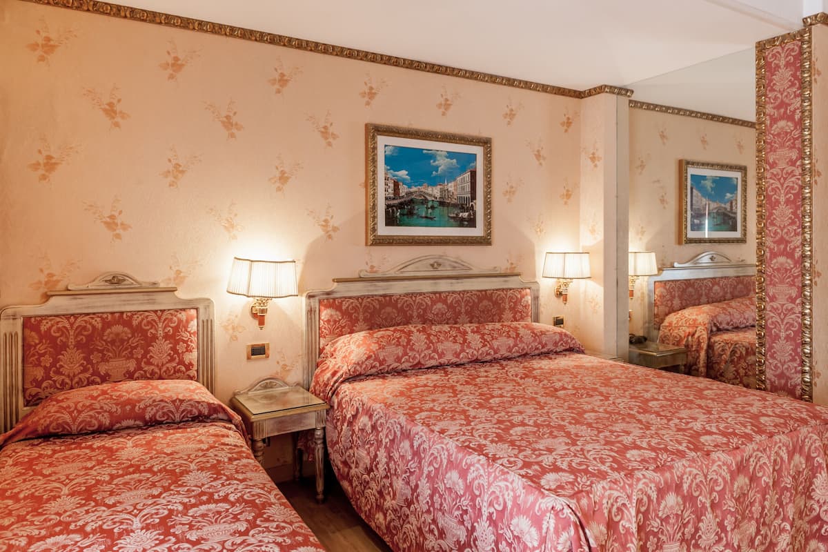 Habitación de hotel con dos camas, papel tapiz floral, un cuadro de Venecia y un espejo con marco decorativo.
