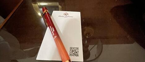 A hotel room with a glass table, a red pen, a white card, and a QR code.