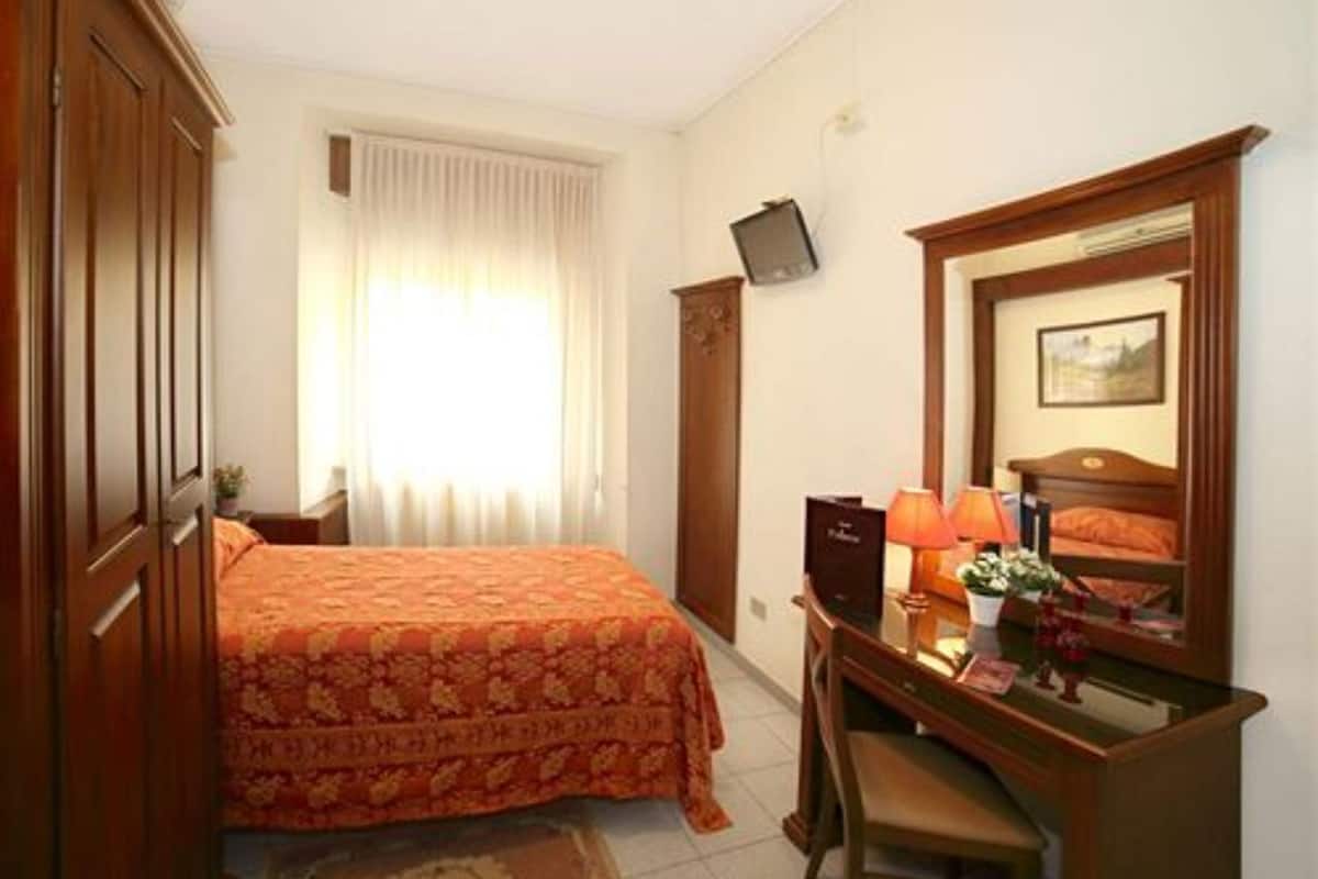 A hotel room with a bed, desk, chair, and a television mounted on the wall.