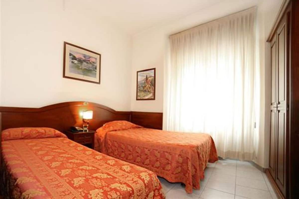 A hotel room with two beds, a nightstand, a lamp, a wardrobe, and two framed pictures on the wall.