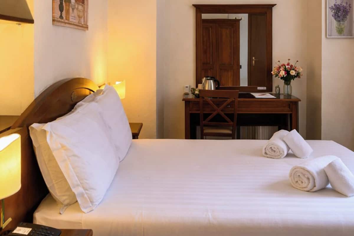A hotel room with a bed, a desk, a chair, a lamp, a telephone, and a mirror.