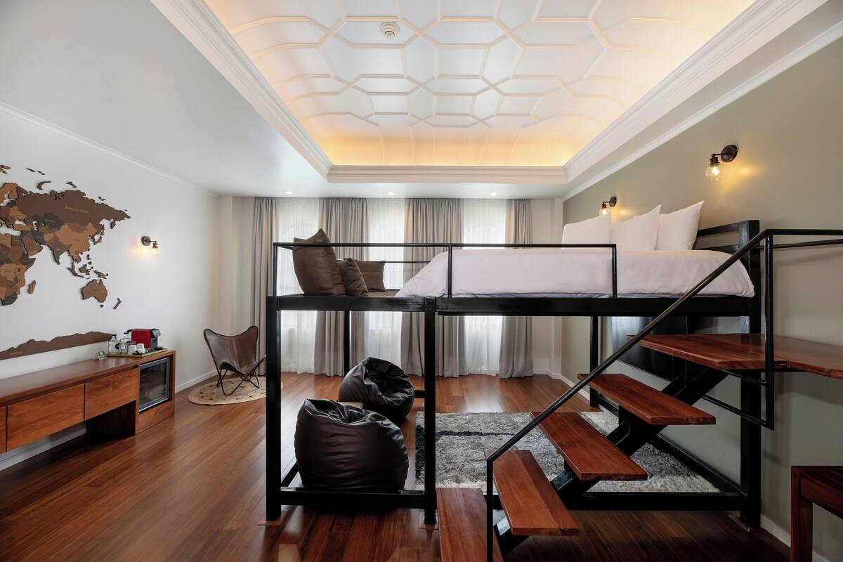 A modern bedroom with a bunk bed, wooden flooring, a world map wall, and a desk with a chair.