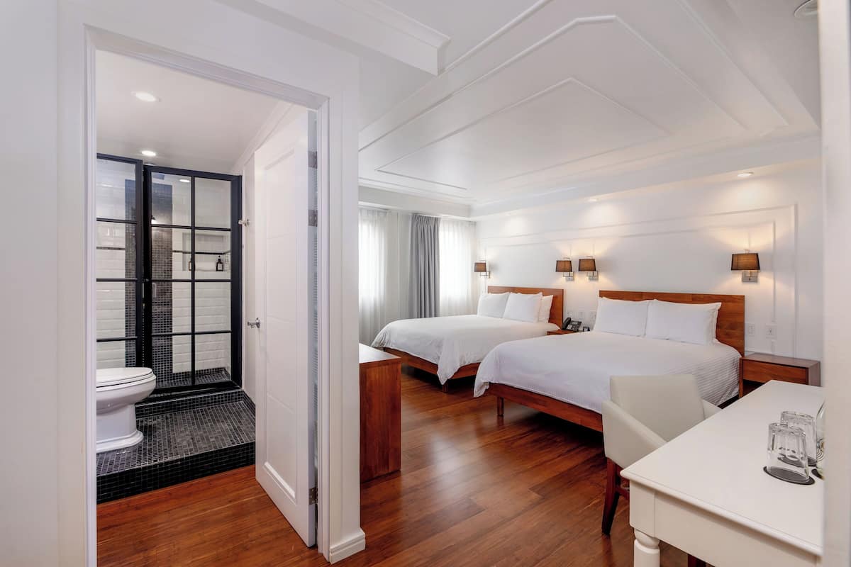 A hotel room with two beds, a desk, and a bathroom with a shower and toilet.
