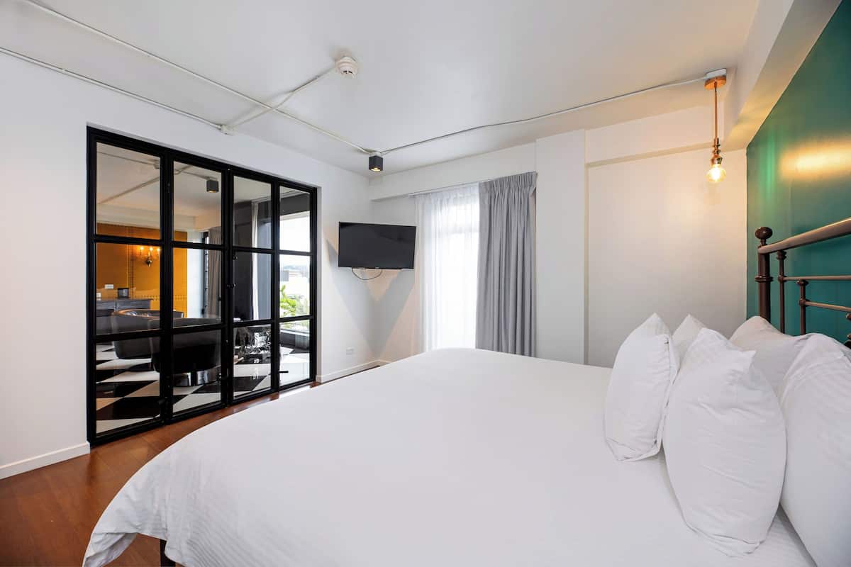A modern hotel room with a large bed, a flat-screen TV mounted on the wall, and a sliding glass door leading to an outdoor area.
