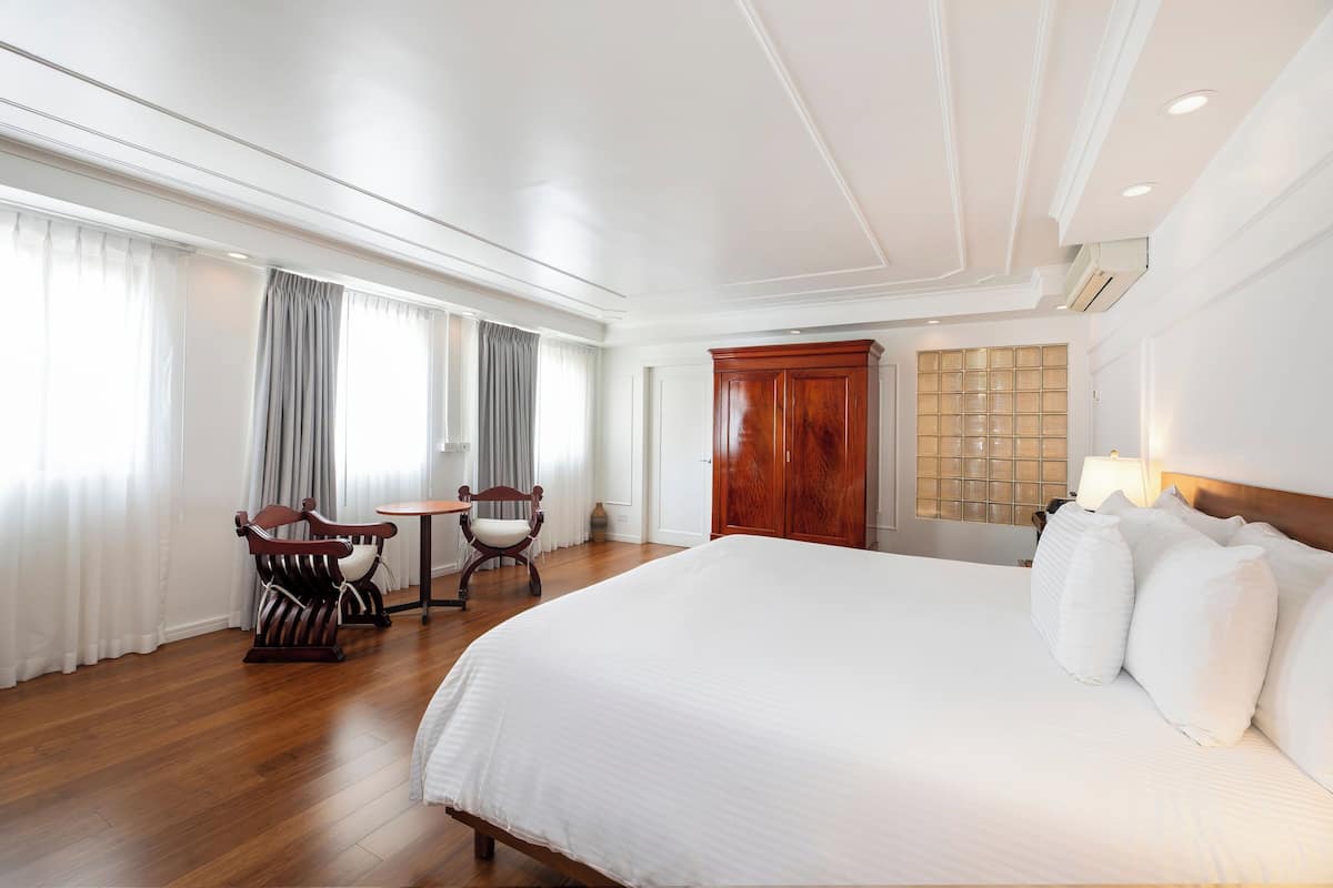 A hotel room with a large bed, wooden floor, a desk with a chair, and a wardrobe.