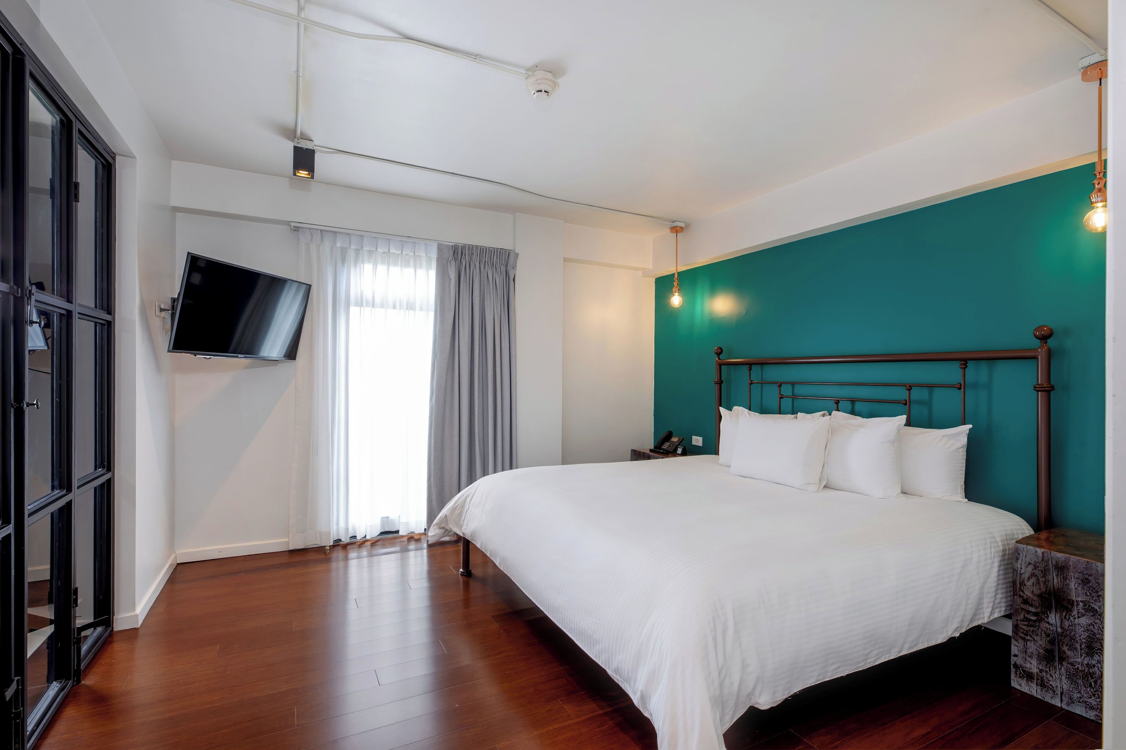 A bedroom with a large bed, a TV mounted on the wall, and a teal accent wall.