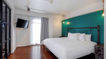A bedroom with a large bed, a TV mounted on the wall, and a teal accent wall.